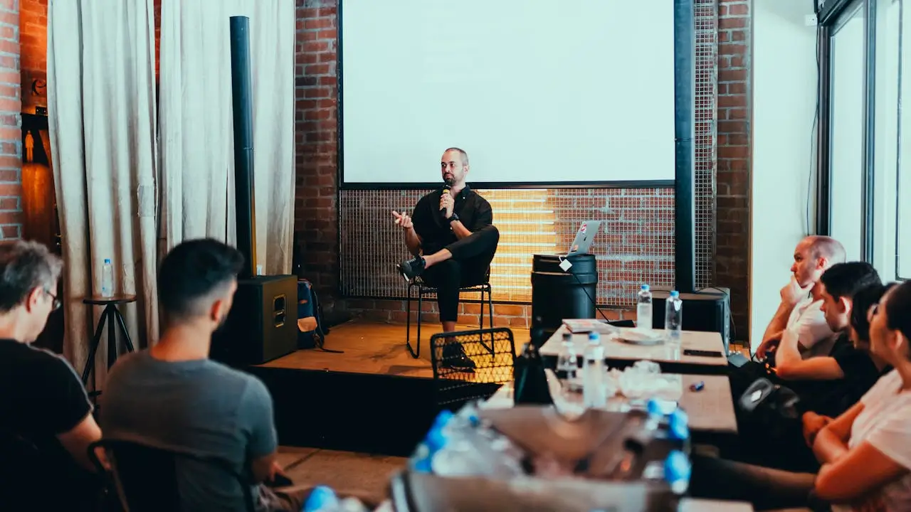 A speaker engages with an audience during a seminar in a modern venue with brick walls and industrial elements.